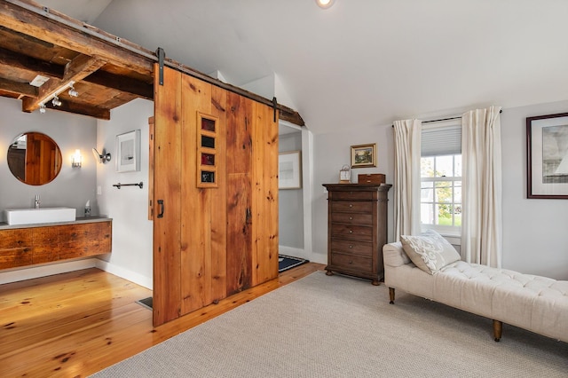 sitting room featuring wood finished floors, lofted ceiling with beams, baseboards, and a barn door