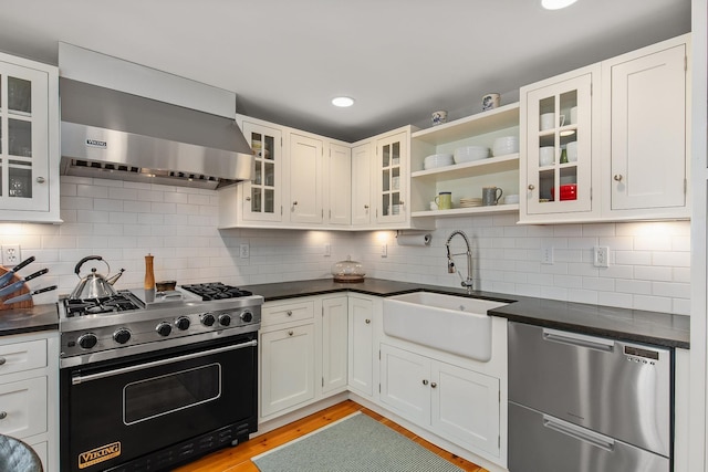 kitchen featuring a sink, exhaust hood, stainless steel dishwasher, dark countertops, and gas range