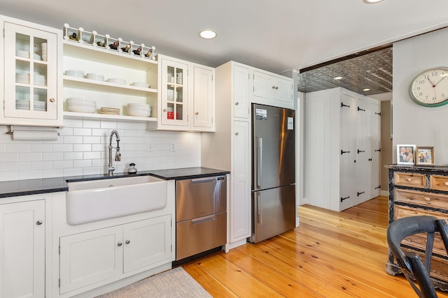 kitchen featuring a sink, white cabinetry, light wood-style floors, appliances with stainless steel finishes, and dark countertops