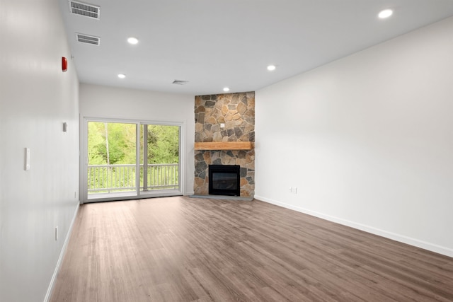 unfurnished living room with a stone fireplace, wood finished floors, visible vents, and baseboards