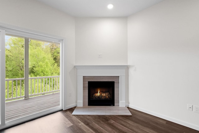 unfurnished living room with recessed lighting, a warm lit fireplace, baseboards, and wood finished floors