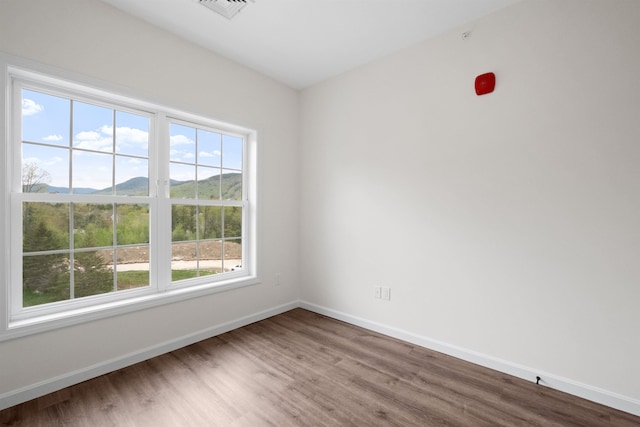 unfurnished room with visible vents, a mountain view, baseboards, and wood finished floors