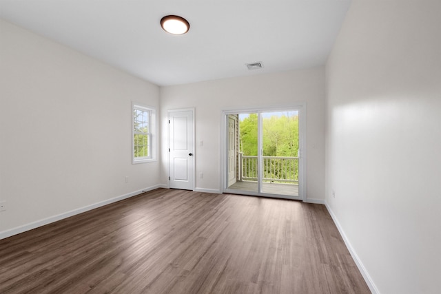 empty room featuring wood finished floors, visible vents, and baseboards