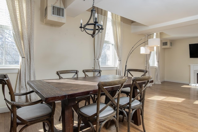 dining space with visible vents, light wood-style floors, a fireplace with flush hearth, a chandelier, and baseboards