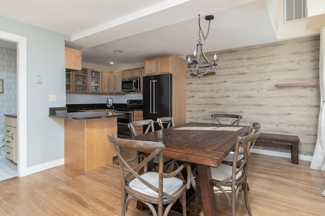 dining room with wooden walls, baseboards, visible vents, light wood-type flooring, and a notable chandelier