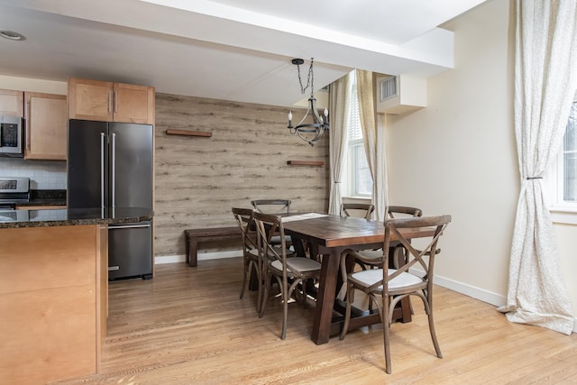 dining area with baseboards, visible vents, wooden walls, and light wood finished floors