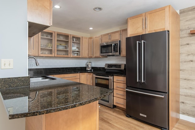 kitchen with dark stone counters, appliances with stainless steel finishes, light brown cabinets, and light wood-style floors