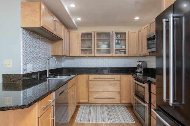 kitchen featuring tasteful backsplash, glass insert cabinets, dark stone countertops, stainless steel appliances, and a sink