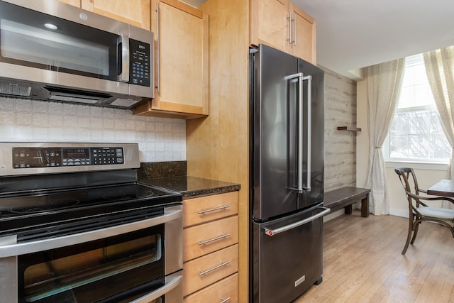 kitchen featuring light brown cabinets, stainless steel appliances, light wood-type flooring, backsplash, and dark stone countertops