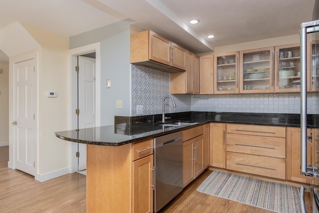 kitchen with tasteful backsplash, stainless steel dishwasher, light wood-style floors, a sink, and dark stone countertops