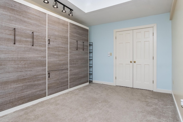 unfurnished bedroom featuring carpet floors, rail lighting, baseboards, and a closet