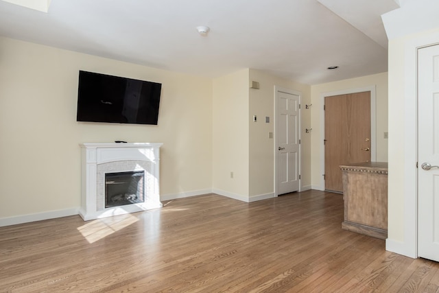 unfurnished living room featuring a glass covered fireplace, wood finished floors, and baseboards