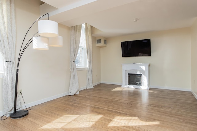 unfurnished living room with a fireplace with flush hearth, baseboards, and wood finished floors