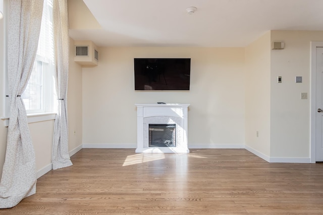 unfurnished living room featuring a glass covered fireplace, visible vents, light wood-style flooring, and baseboards