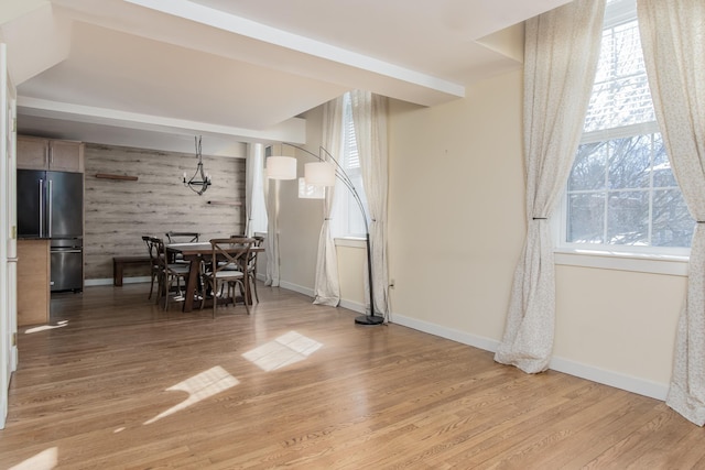 dining area featuring an accent wall, wood walls, light wood-type flooring, and baseboards