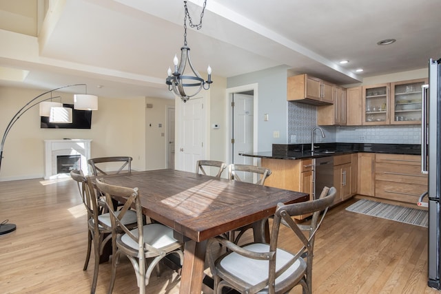 dining area with light wood-style flooring, a fireplace, a chandelier, and baseboards