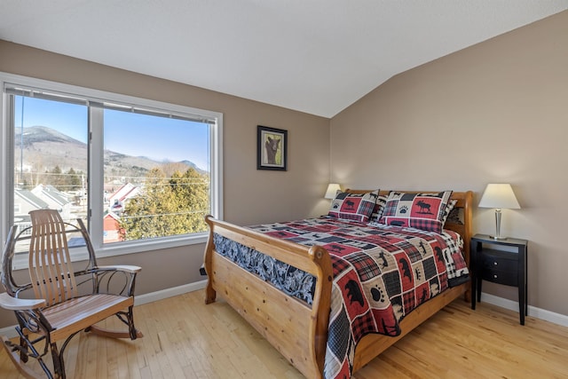 bedroom with lofted ceiling, light wood-type flooring, a mountain view, and baseboards