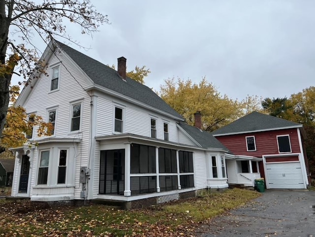 back of property with a garage, a chimney, and a sunroom