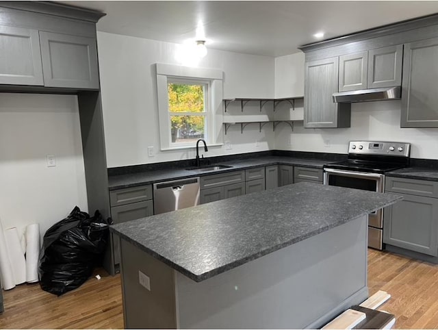 kitchen with under cabinet range hood, a sink, appliances with stainless steel finishes, light wood-type flooring, and gray cabinets