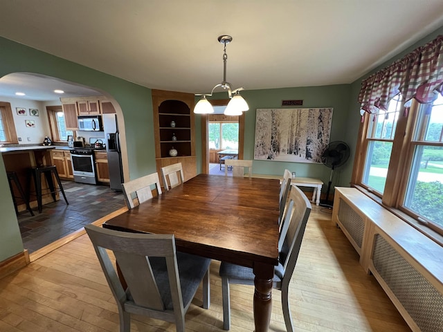 dining area featuring arched walkways, hardwood / wood-style flooring, and radiator