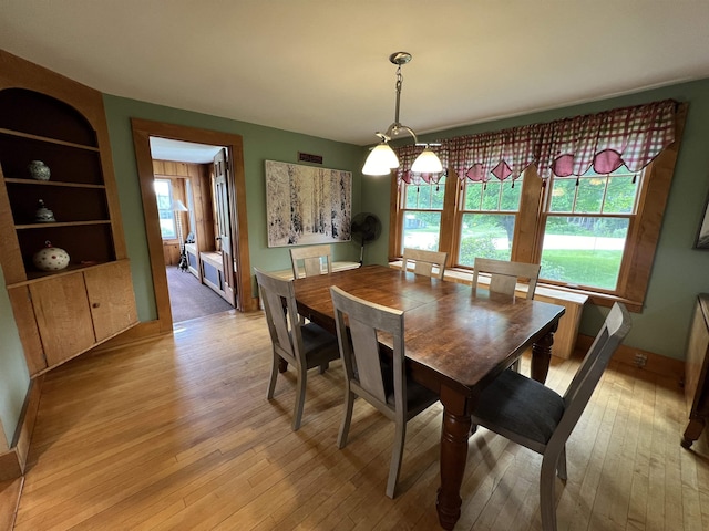 dining area with built in shelves, a notable chandelier, and light wood-style flooring