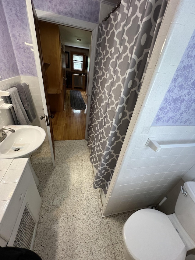 full bathroom with speckled floor, a wainscoted wall, tile walls, and wallpapered walls