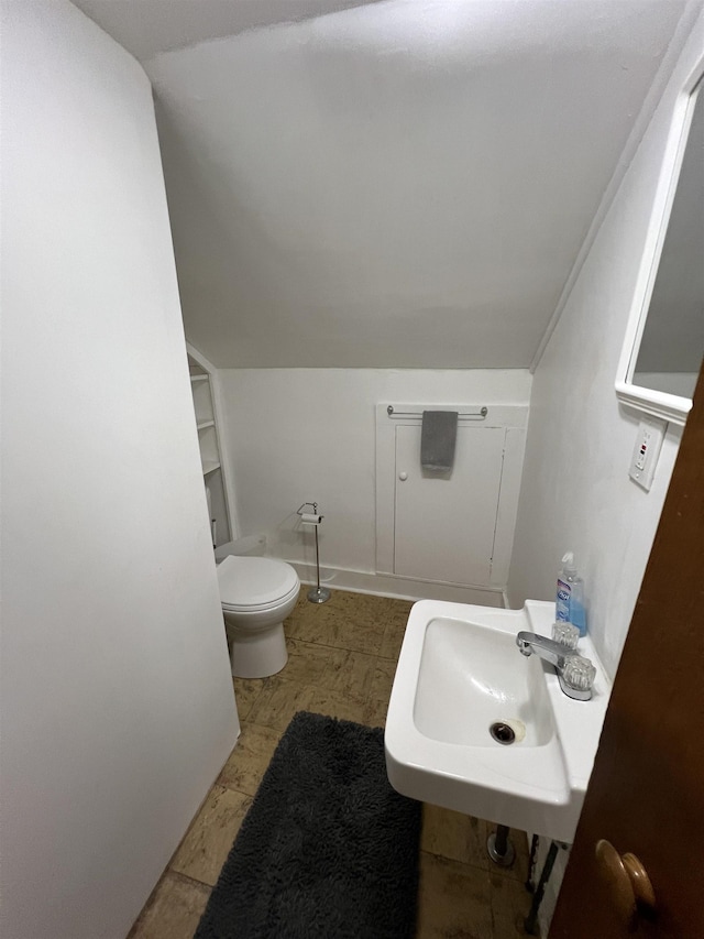 bathroom with lofted ceiling, baseboards, toilet, and a sink