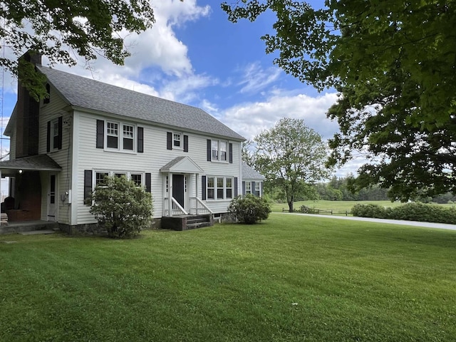 colonial home featuring a shingled roof, a front yard, and a chimney