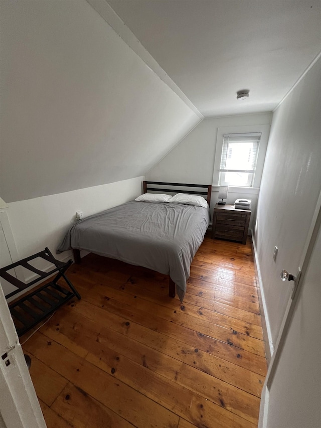 bedroom featuring hardwood / wood-style flooring, baseboards, and vaulted ceiling