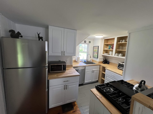 kitchen with white cabinets, butcher block countertops, stainless steel appliances, open shelves, and a sink