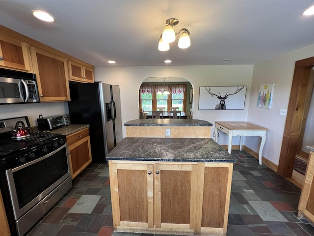 kitchen with arched walkways, stone tile floors, appliances with stainless steel finishes, a center island, and dark countertops