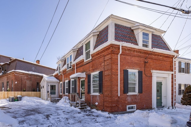 view of front of home with brick siding, mansard roof, and fence