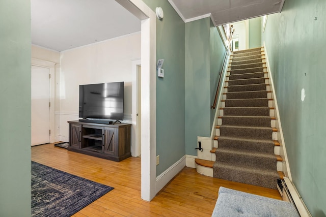 staircase with baseboards, crown molding, a baseboard heating unit, and hardwood / wood-style floors