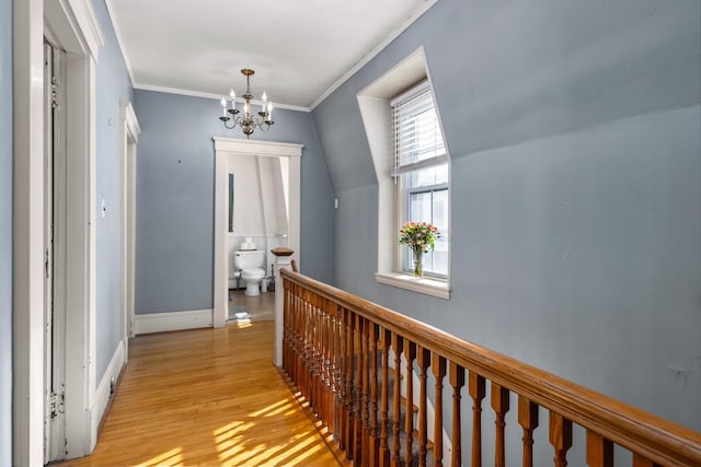 hall with a notable chandelier, an upstairs landing, baseboards, light wood finished floors, and crown molding