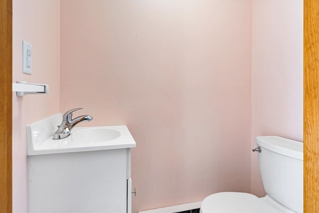 half bathroom featuring toilet, a baseboard heating unit, and vanity