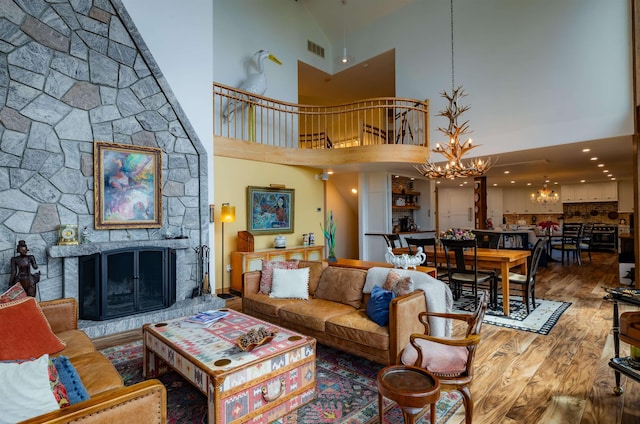 living room featuring a stone fireplace, a high ceiling, wood finished floors, visible vents, and an inviting chandelier