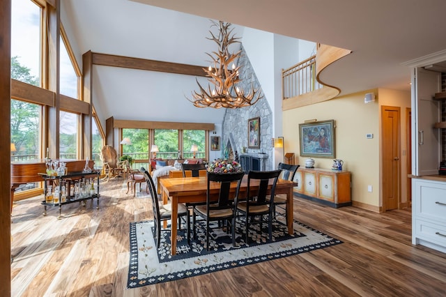 dining area featuring baseboards, wood finished floors, a high ceiling, a fireplace, and a notable chandelier