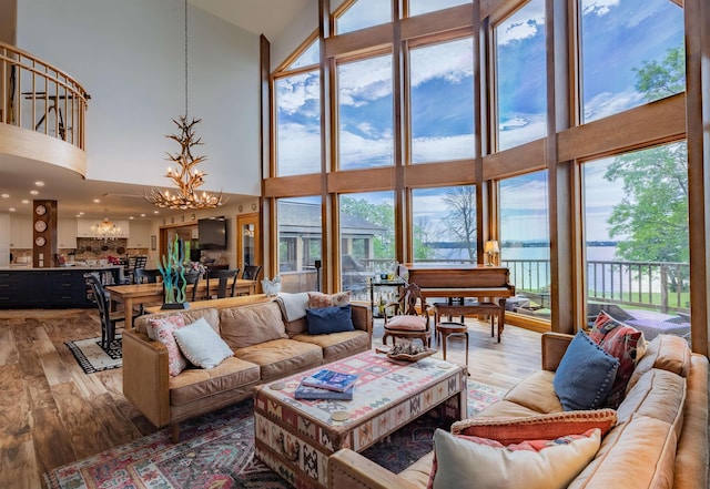 living area featuring a chandelier, a high ceiling, a wall of windows, and light wood-style flooring