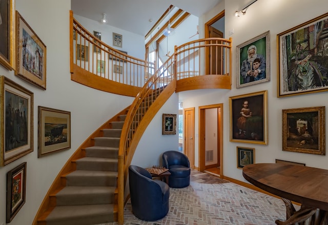 stairway featuring a towering ceiling, brick floor, baseboards, and visible vents