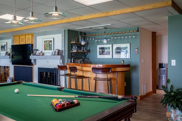 rec room featuring a paneled ceiling, a brick fireplace, a dry bar, and wood finished floors