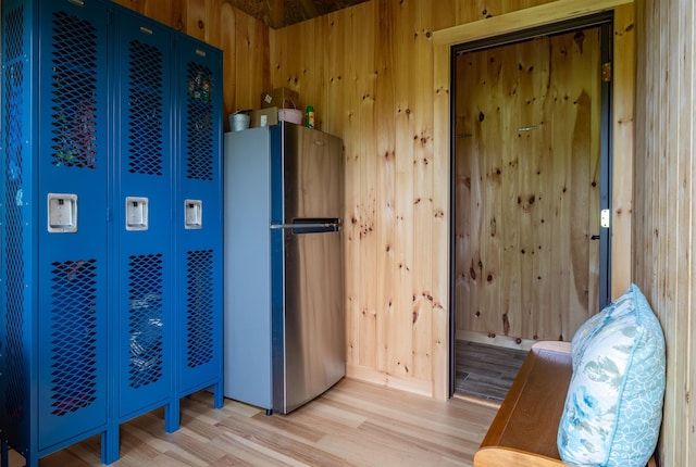 kitchen with light wood-style flooring, freestanding refrigerator, and wooden walls