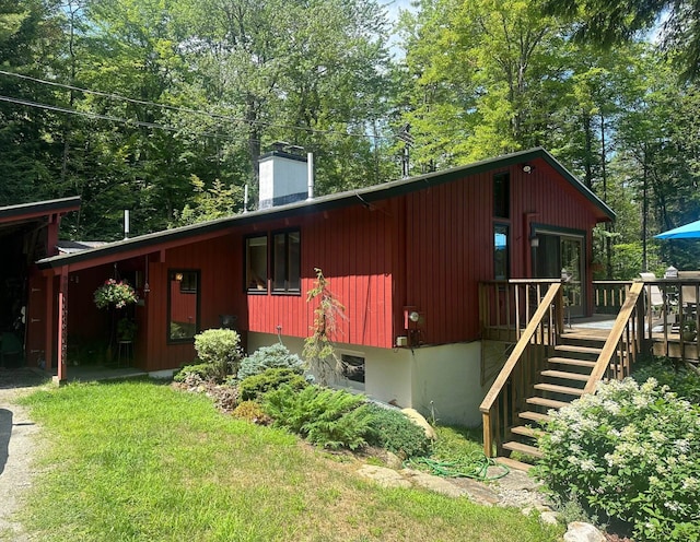 view of front of house featuring a deck, a front yard, a chimney, and stairs