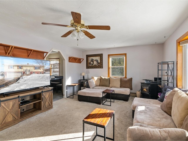 living room featuring ceiling fan, a baseboard heating unit, carpet flooring, and a wood stove