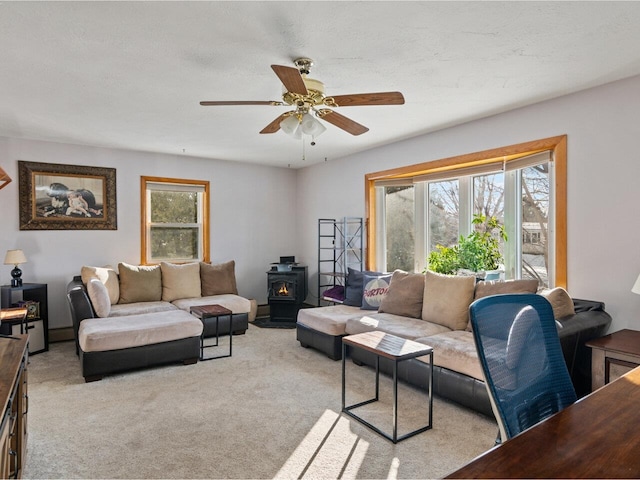 living room with ceiling fan, a wood stove, and light colored carpet