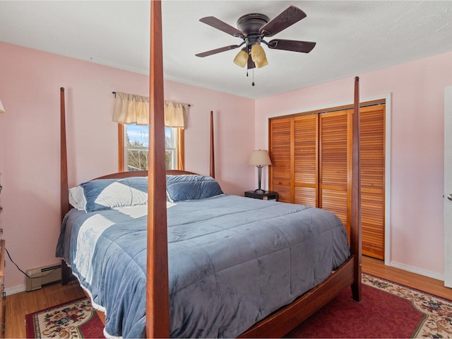 bedroom featuring a baseboard radiator, a closet, ceiling fan, wood finished floors, and baseboards