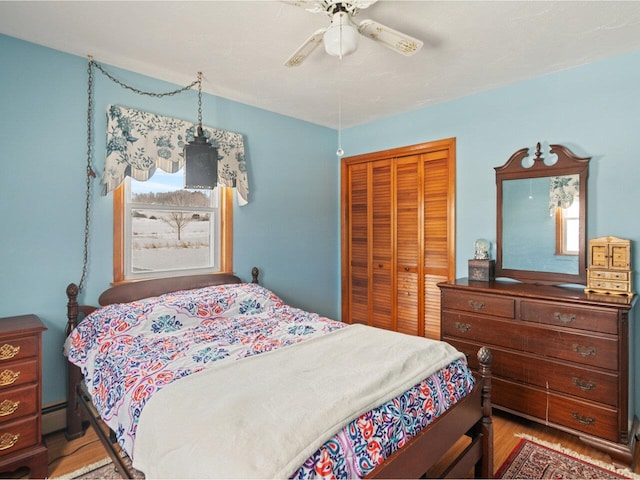 bedroom with ceiling fan, a closet, a baseboard radiator, and wood finished floors