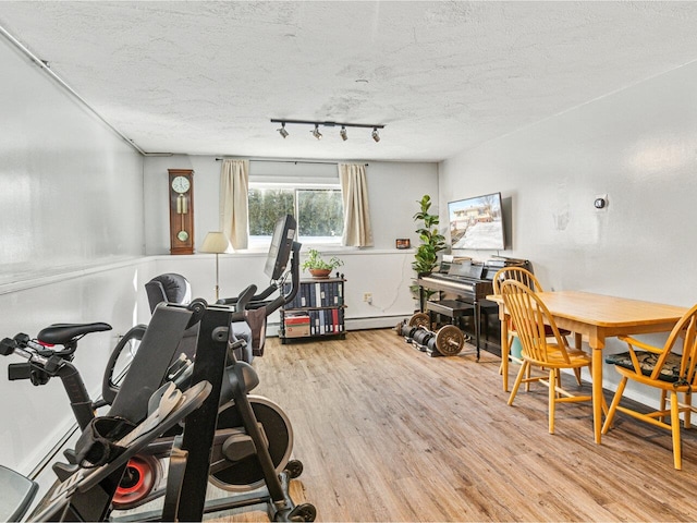 exercise area featuring a baseboard radiator, a textured ceiling, and wood finished floors