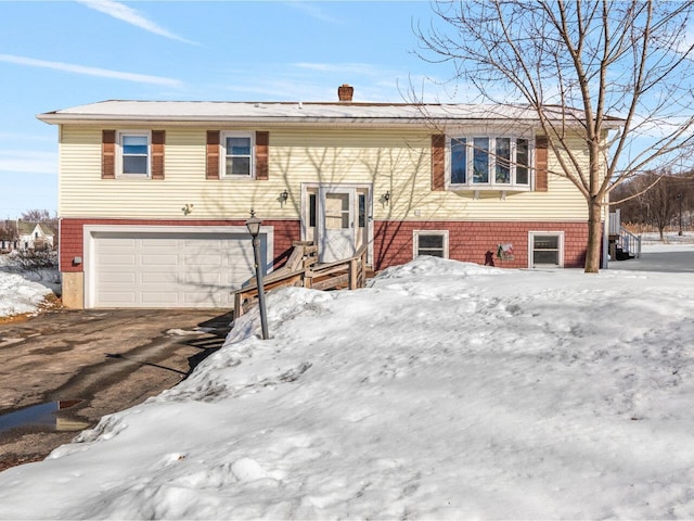 bi-level home featuring a garage, a chimney, and aphalt driveway