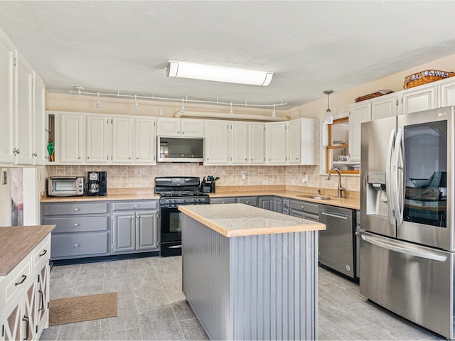 kitchen with stainless steel appliances, decorative backsplash, gray cabinetry, a sink, and a kitchen island