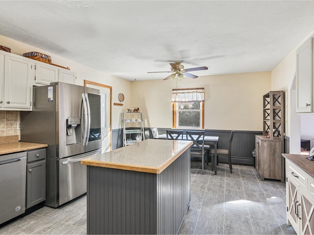 kitchen featuring white cabinets, a wainscoted wall, ceiling fan, appliances with stainless steel finishes, and a center island